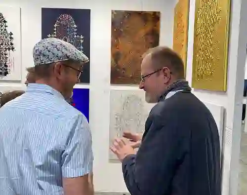 Künstler vor seinen ausgestellten Werken im Gespräch mit einem interessiertem Kunstmesse Besucher.